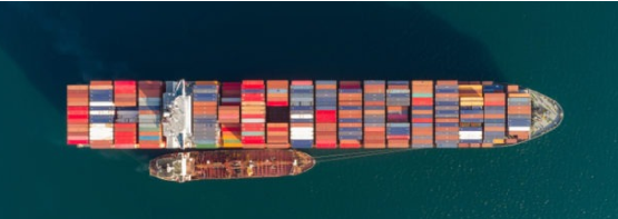 Aerial view of a large cargo ship fully loaded with colorful containers, sailing through calm blue waters, powered by bunker fuel.
